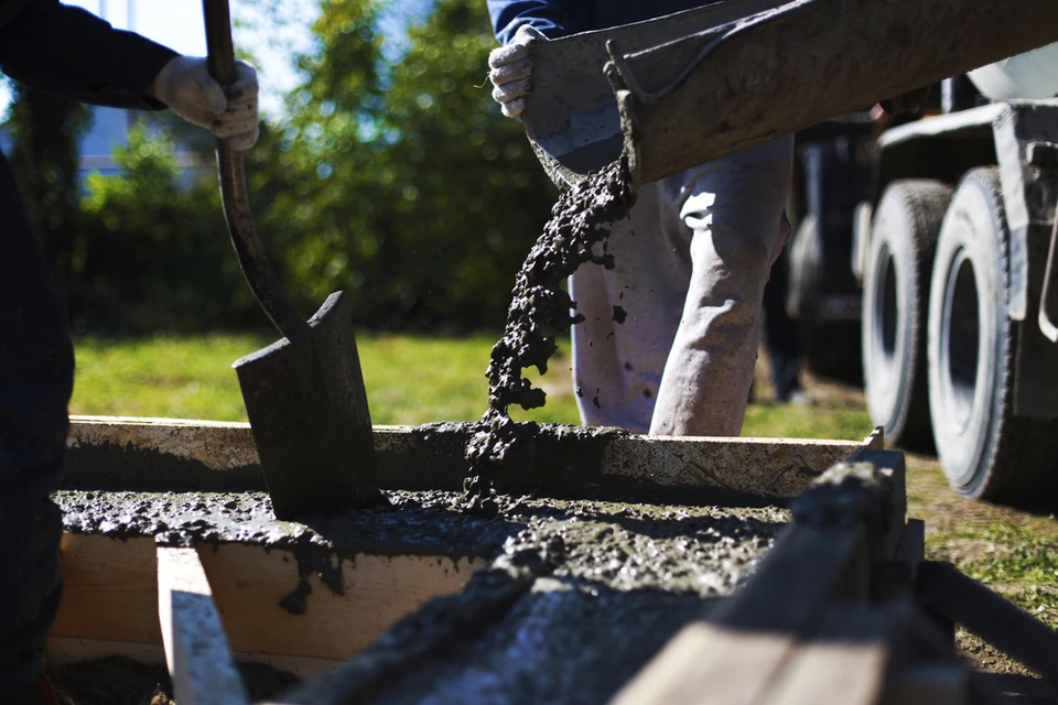 Chantier ext&eacute;rieur avec ouvrier versant du b&eacute;ton frais depuis une benne dans un coffrage en bois