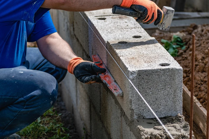 Ouvrier en bâtiment travaillant sur façade extérieure depuis échafaudage, rénovant mur en pierre avec outil de grattage