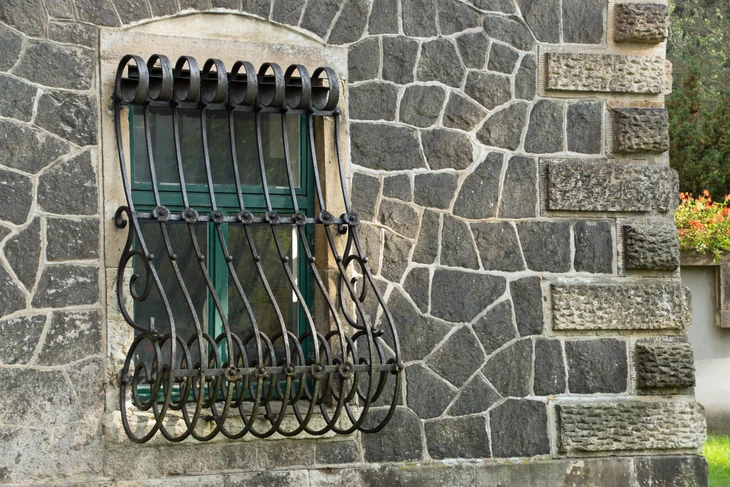 Maçon expérimenté en tenue de travail effectuant un remontage de mur en pierre ancienne, utilisant ses outils traditionnels (truelle, marteau, niveau), avec des pierres appareillées visibles en arrière-plan. La scène montre le travail détaillé, la maîtrise technique et le respect des matériaux anciens, dans un style photographique naturel et professionnel qui témoigne du savoir-faire artisanal.