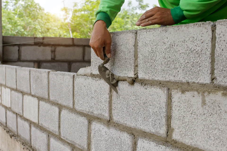 Un maçon travaille sur des blocs pour construire un mur sur un chantier de construction avec du béton, une truelle, un niveau et une meule