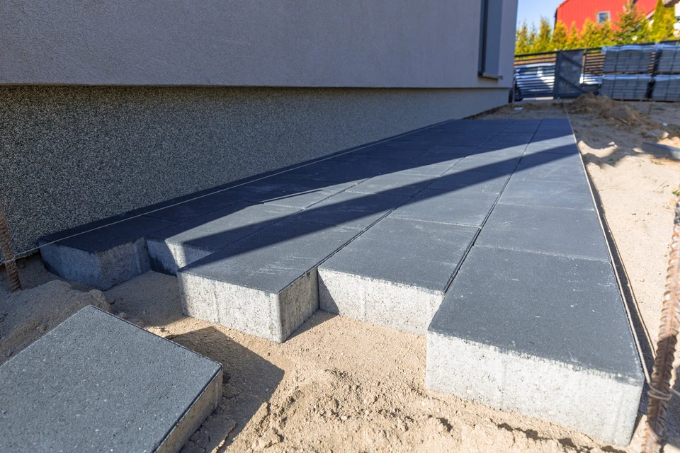 Chantier extérieur avec ouvriers posant des dalles de béton sur une surface préparée