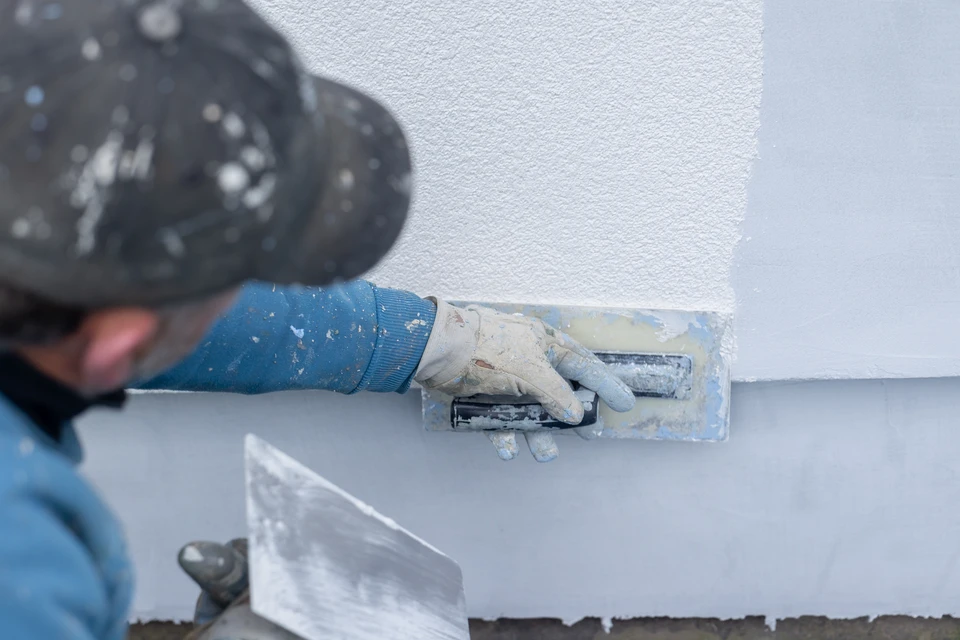 Ouvrier en bâtiment applique un enduit mural à la spatule sur parpaings